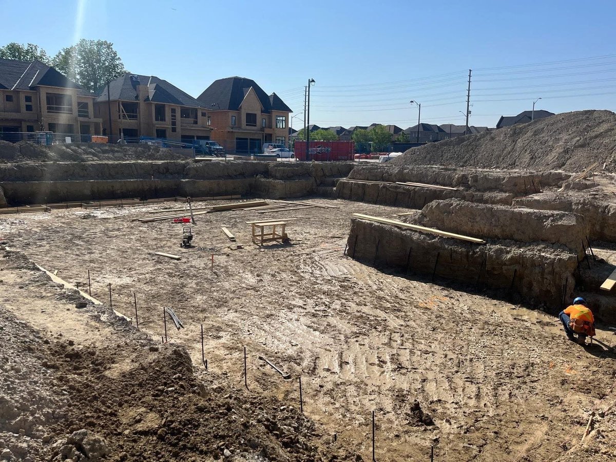 Construction site with excavated foundation trenches, newly built residential homes, and construction equipment under development — MAY Engineering engineering letters Ontario