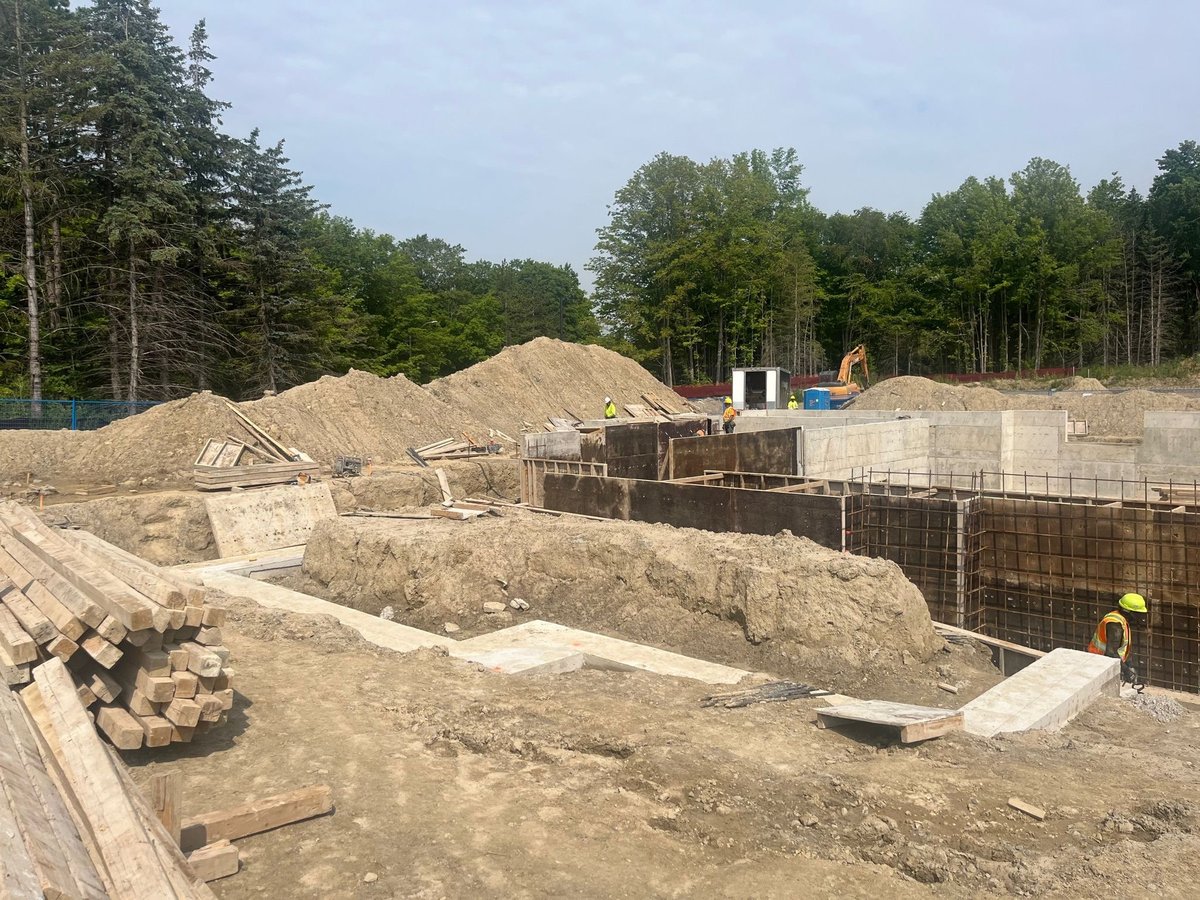 Active construction site with excavation equipment, concrete foundation forms, dirt mounds, and workers — MAY Engineering construction management Ontario contractor coordination