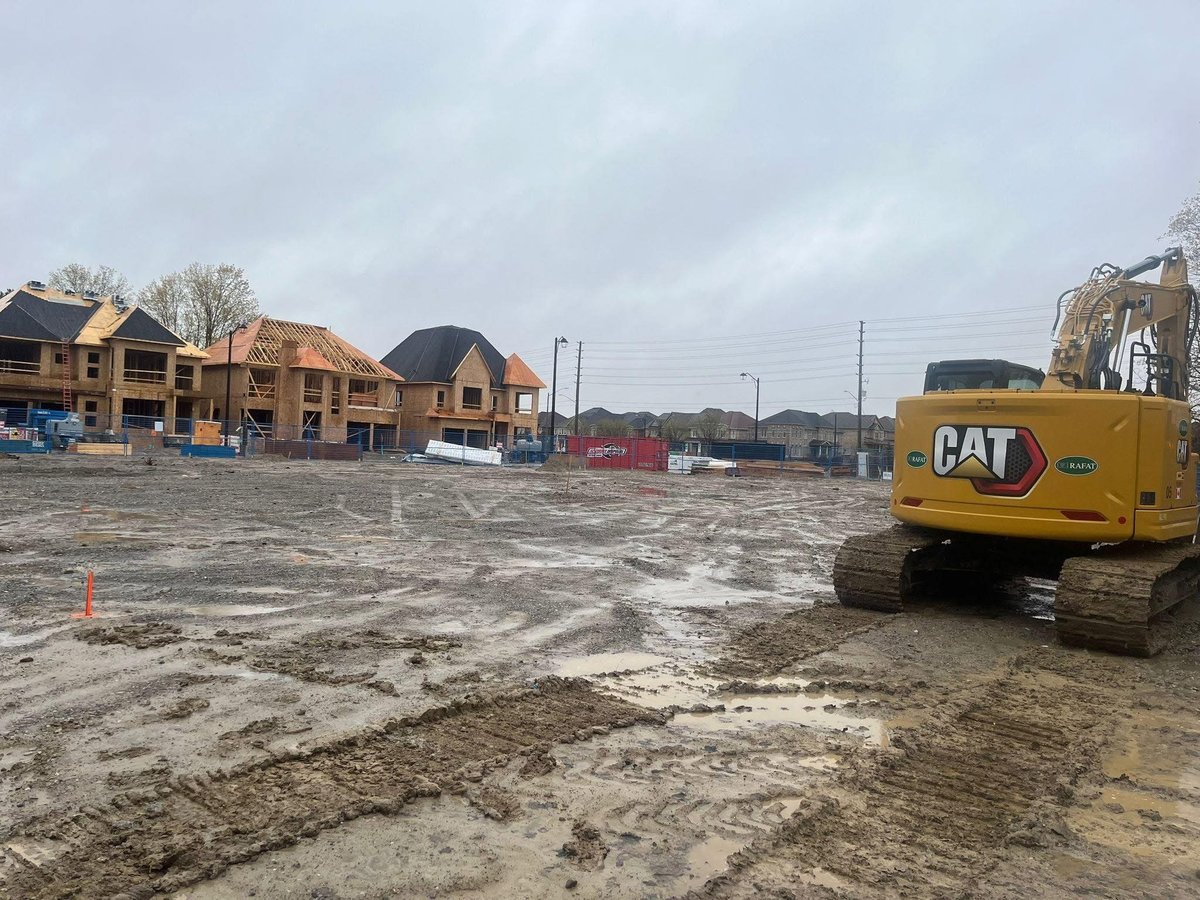CAT excavator on a muddy construction site with residential homes in background — construction management site prep project in Vaughan Ontario — MAY Engineering Inc.